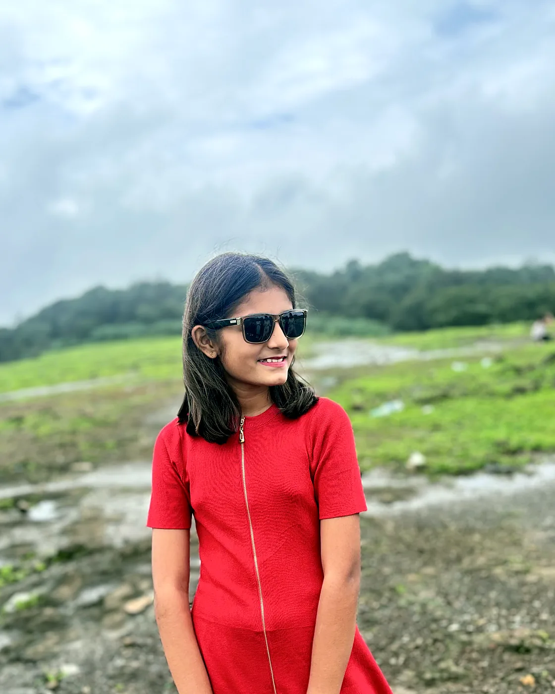 Nishtha in a red dress on a green hillside