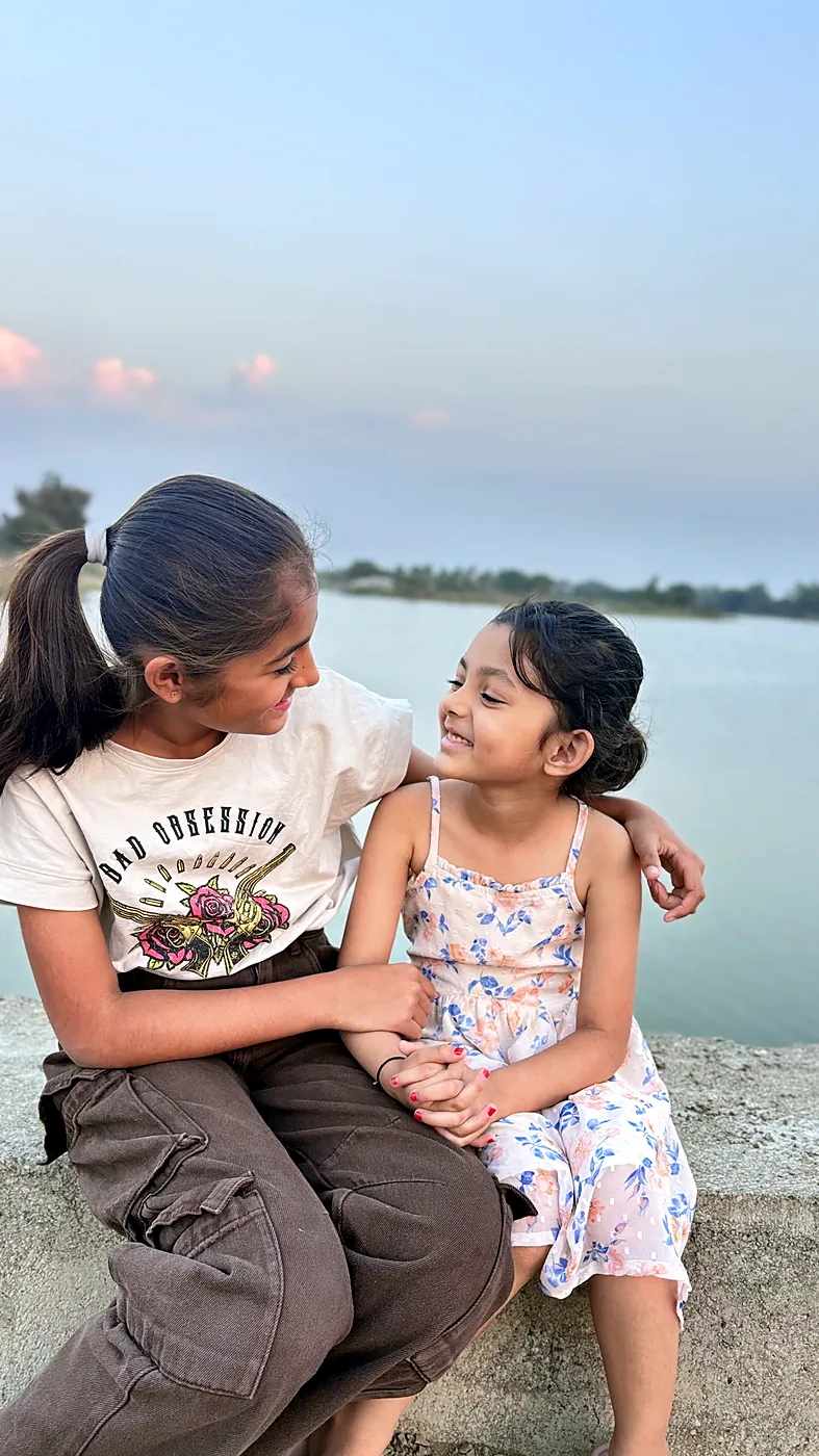 The sisters crouched together by the water at sunset